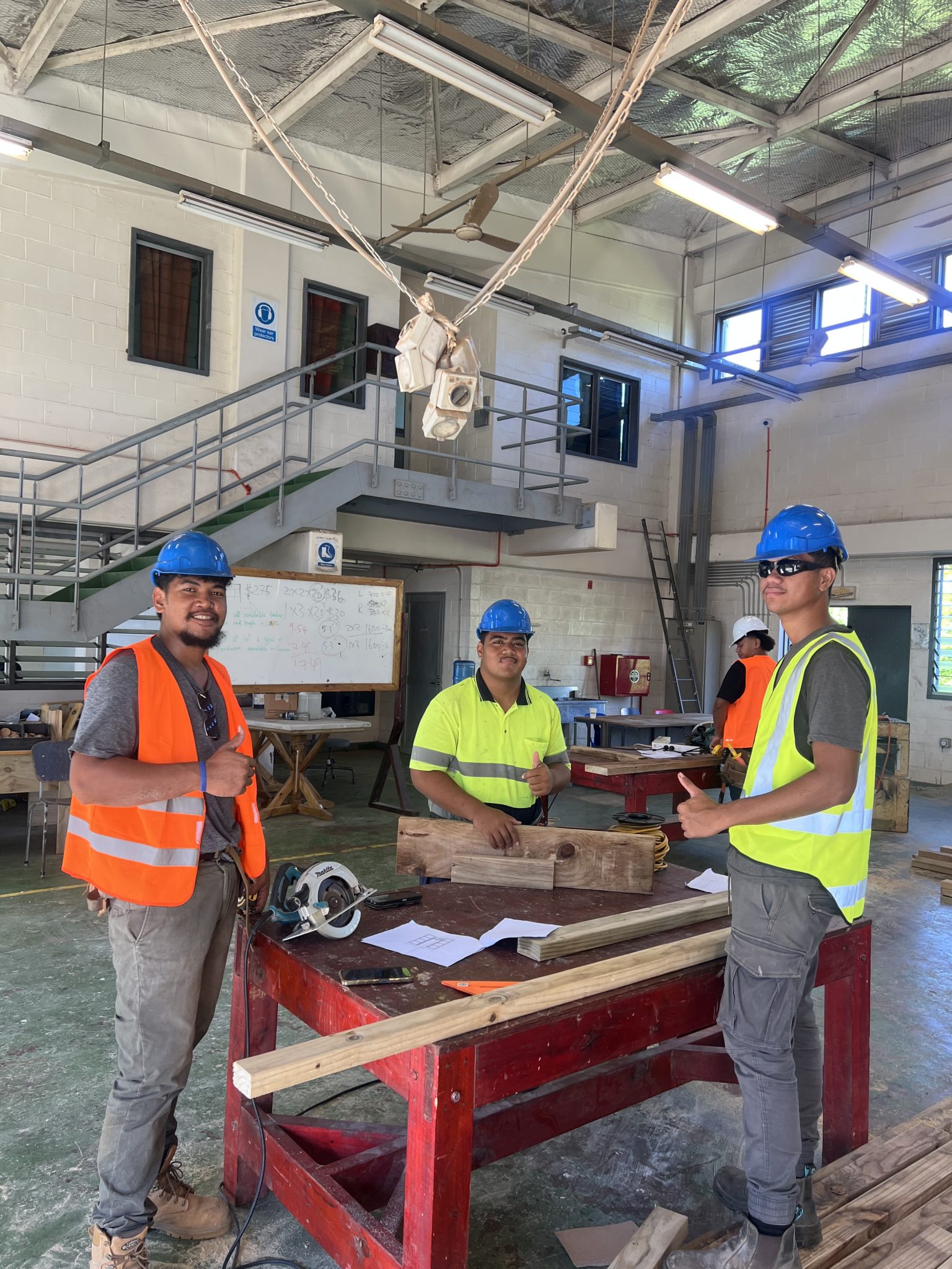 Three carpenters with their tools at a workbench inside the carpentry workshop.