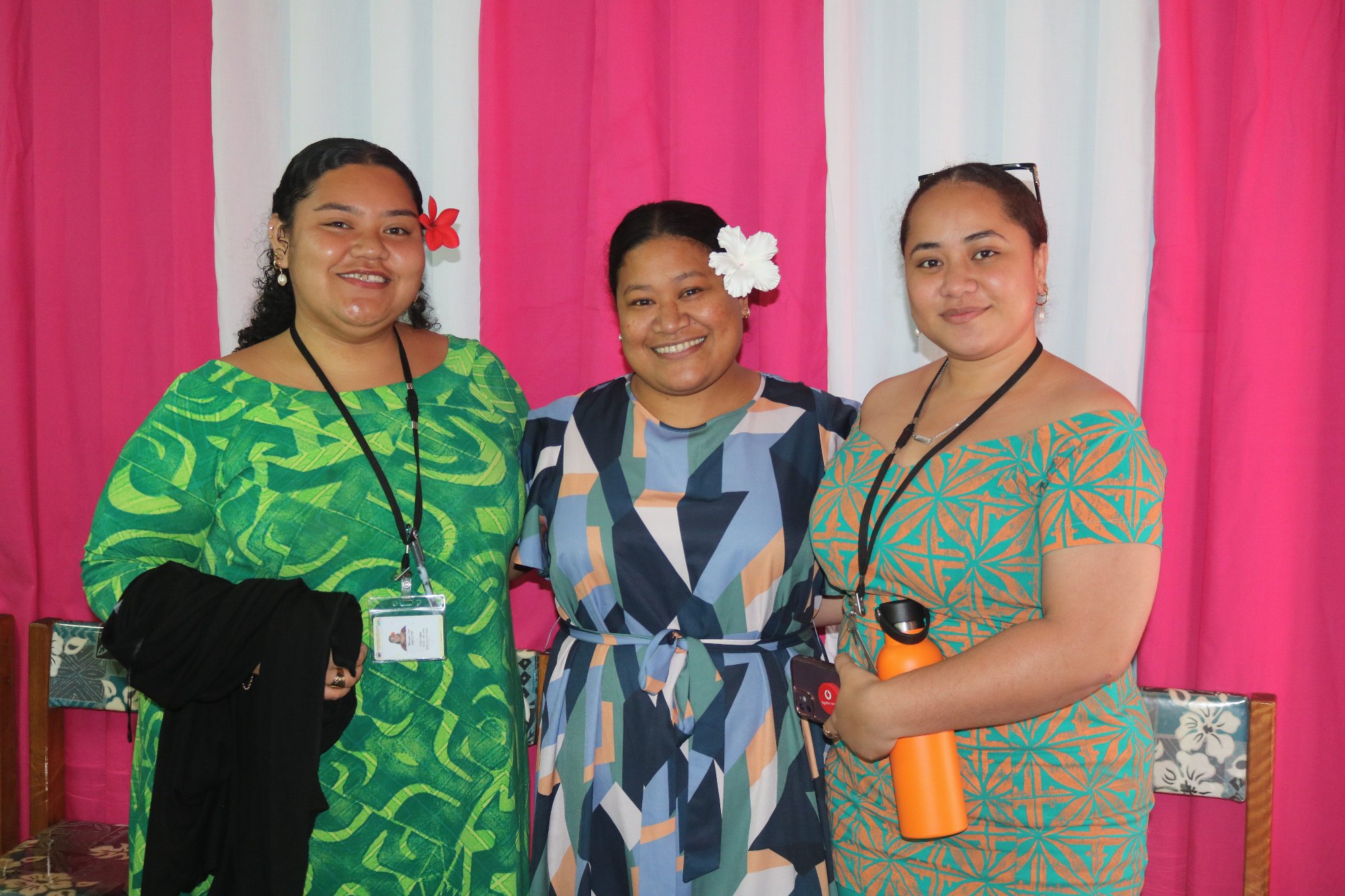 Three MCIL staff smile together in front of pink and white curtains